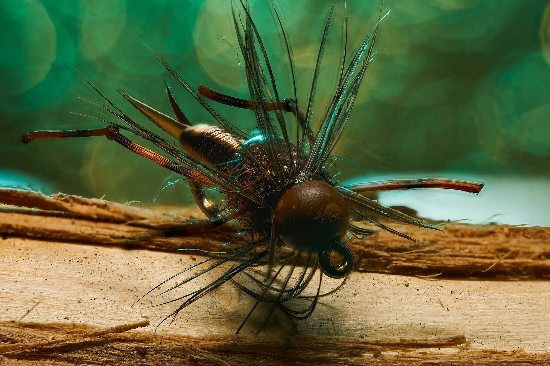 Macro product photo of a dark teal fishing fly resting on a textured wood surface