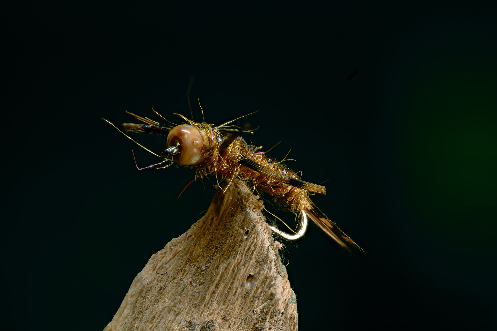 Macro product photo of a cream-colored fishing fly mounted on a wood perch, dark background