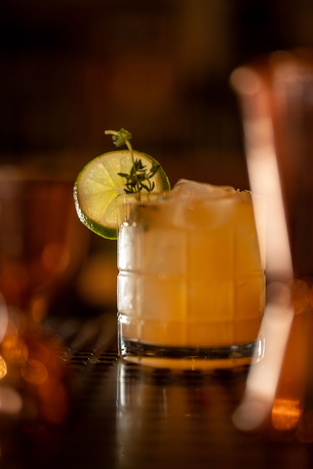 Gold Rush cocktail garnished with a lime wheel and thyme, at Pretty Neat Bar