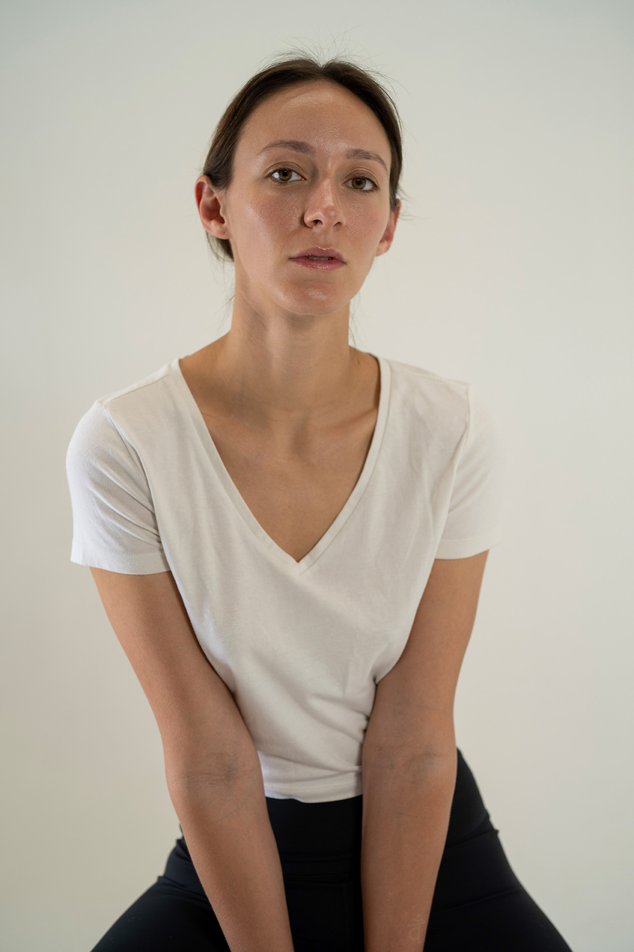 Model portfolio digital, front-facing with a slight head tilt, white v-neck t-shirt, neutral studio background