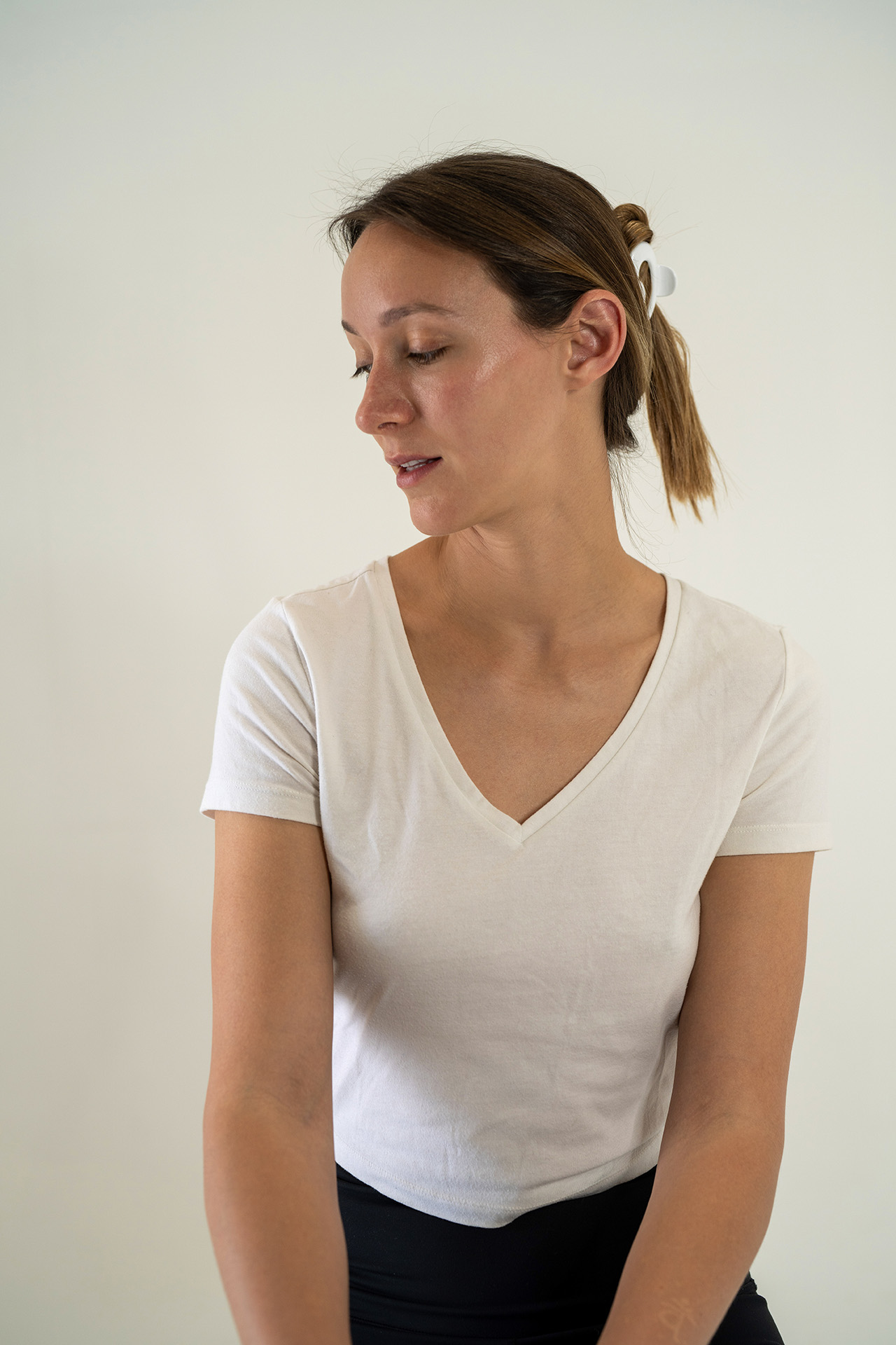 Model portfolio digital looking downward in a white v-neck t-shirt, soft studio lighting