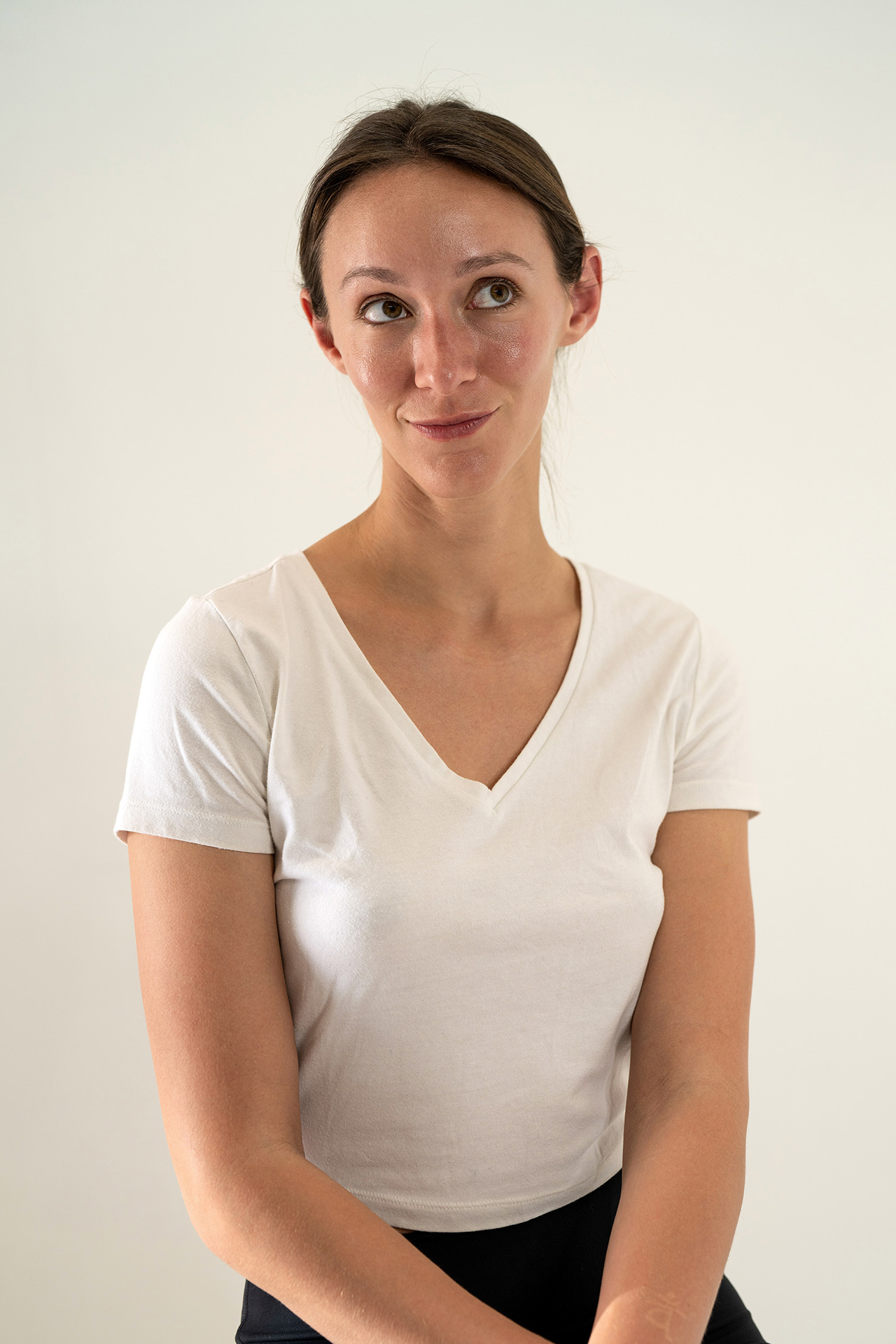 Model portfolio digital, body facing forward with head turned to the side and a slight smile, white v-neck t-shirt, neutral background