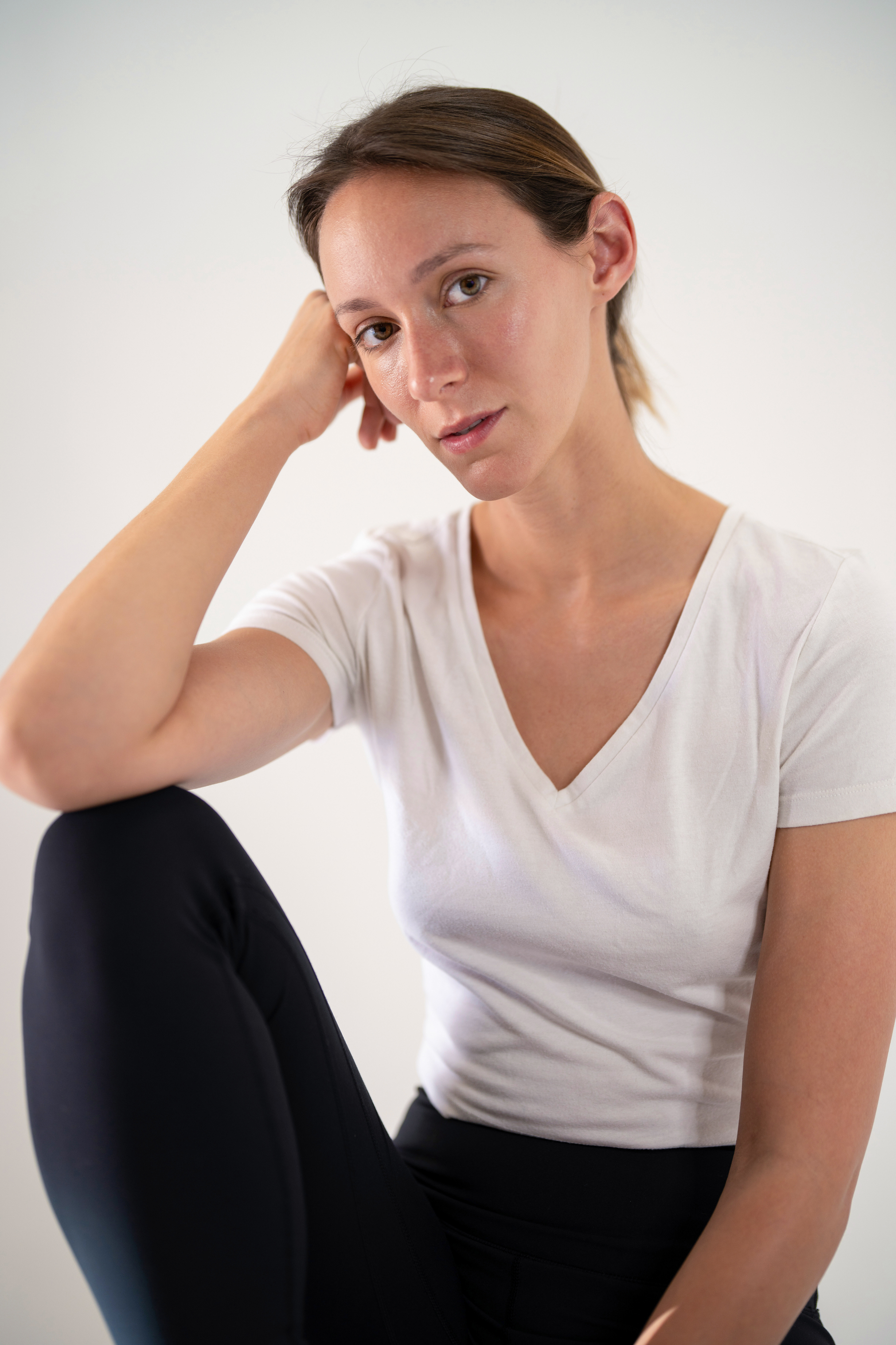Seated model portfolio digital with hand resting near her head, white v-neck t-shirt, neutral background