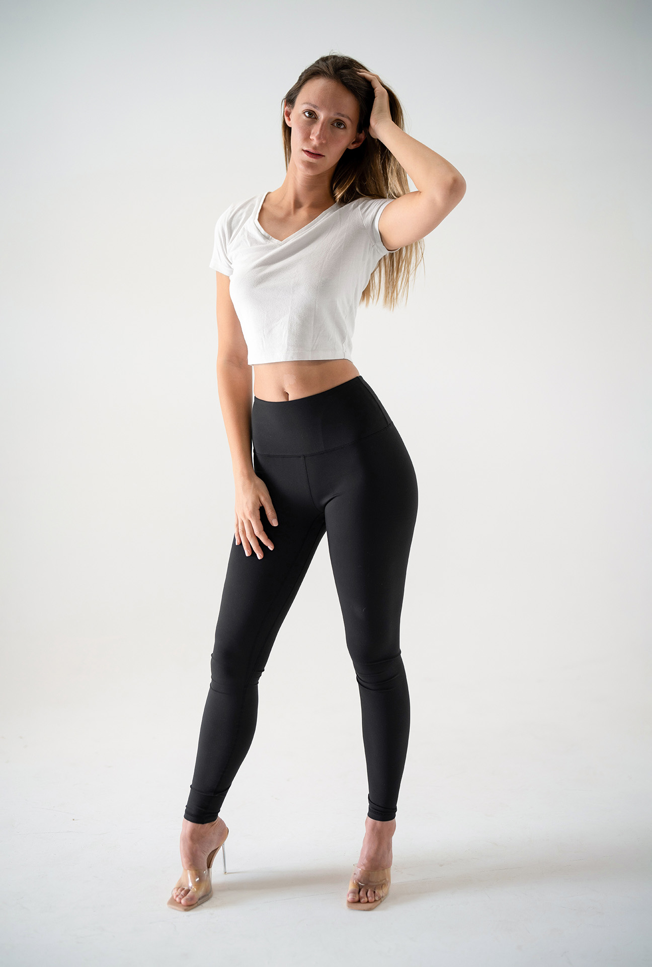 Full-body model portfolio digital with one arm raised touching her hair, black leggings