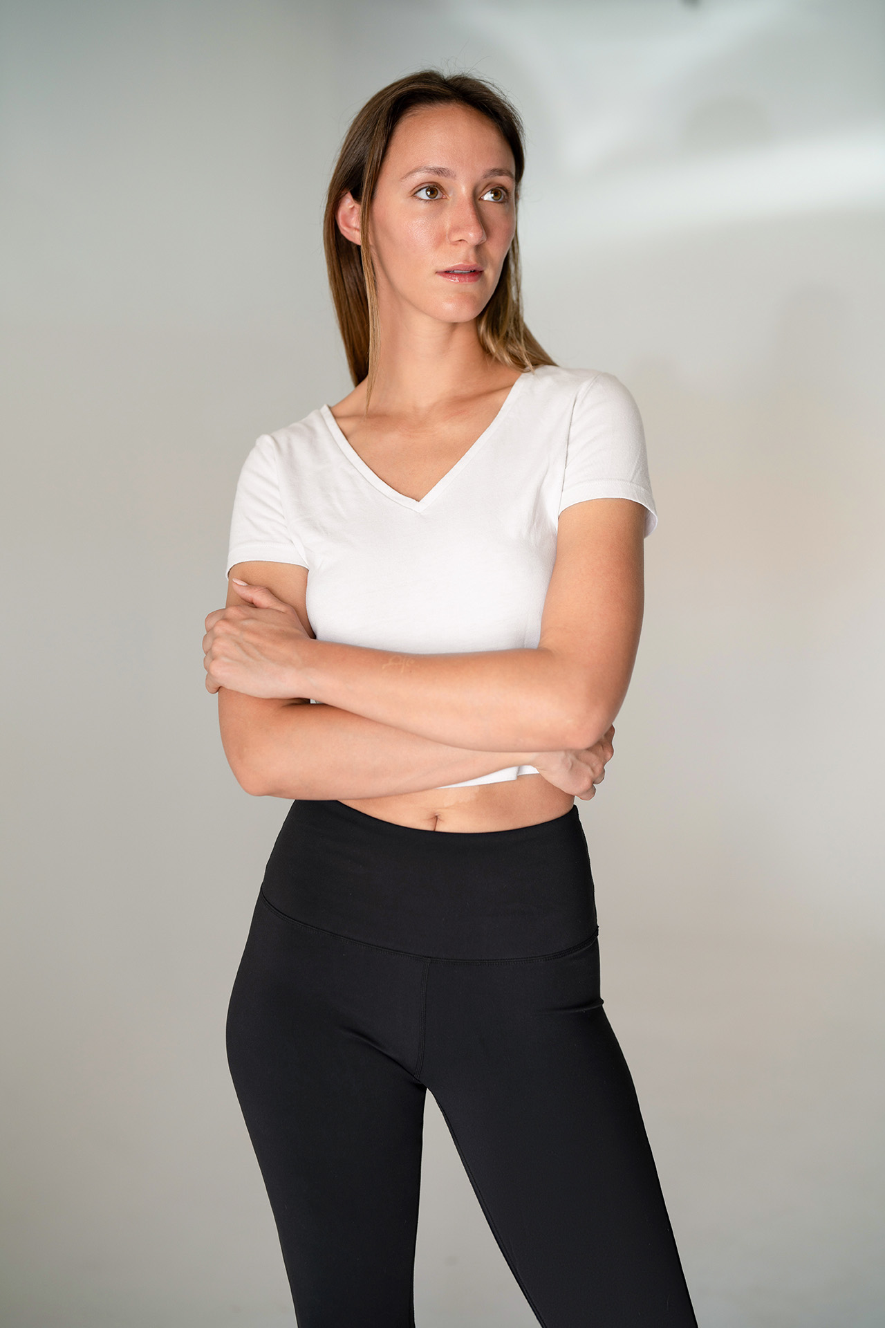 Model portfolio digital, cropped just above the knees, arms crossed, front-facing, white v-neck top and black leggings