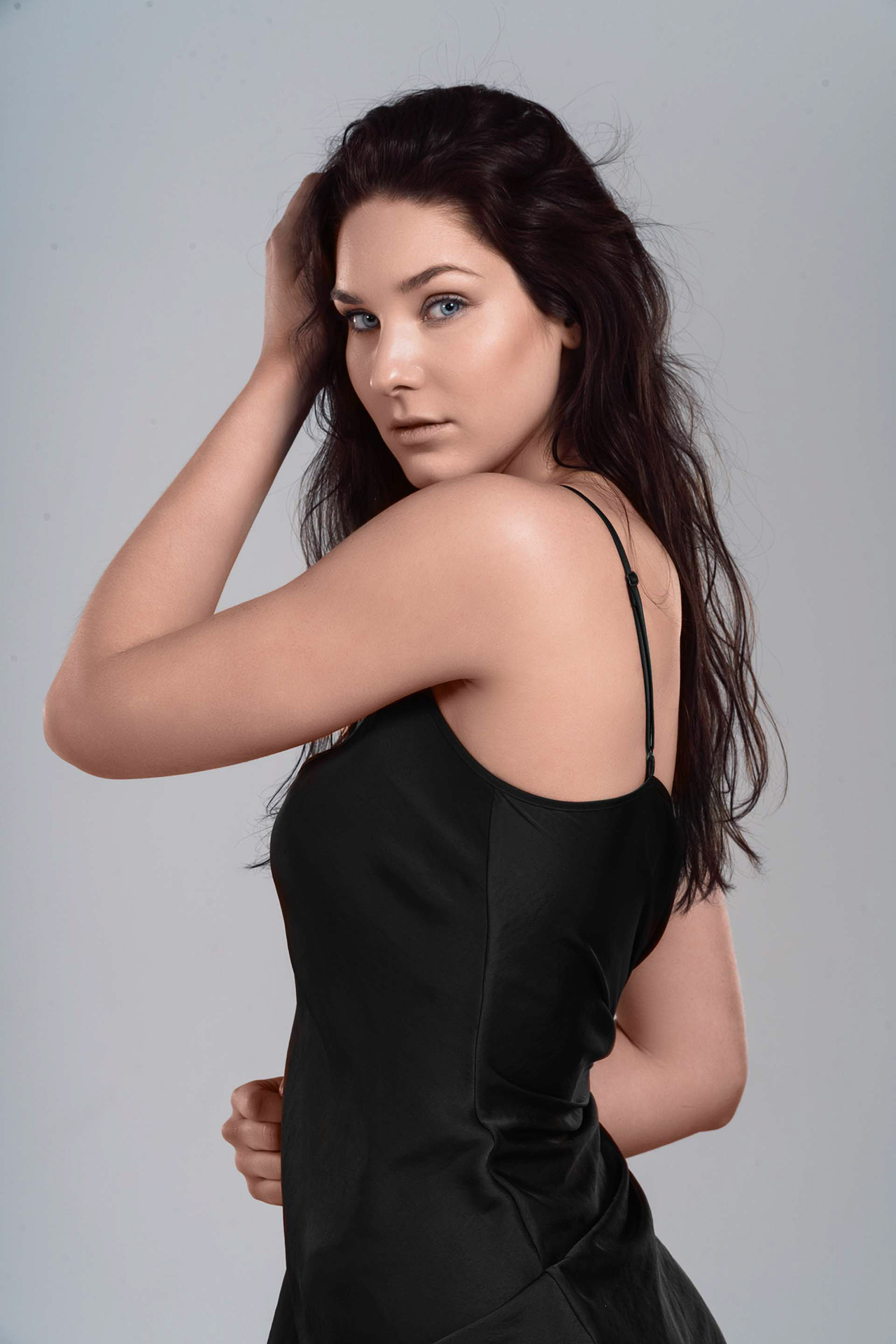 Model glancing over her shoulder in a black dress against a gray studio backdrop, Denver portrait photography
