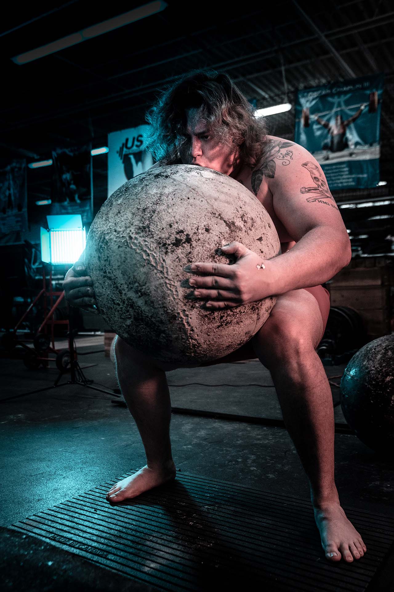 Strongman athlete lifting an atlas stone in a dramatic industrial gym, Aurora & Denver sports photography
