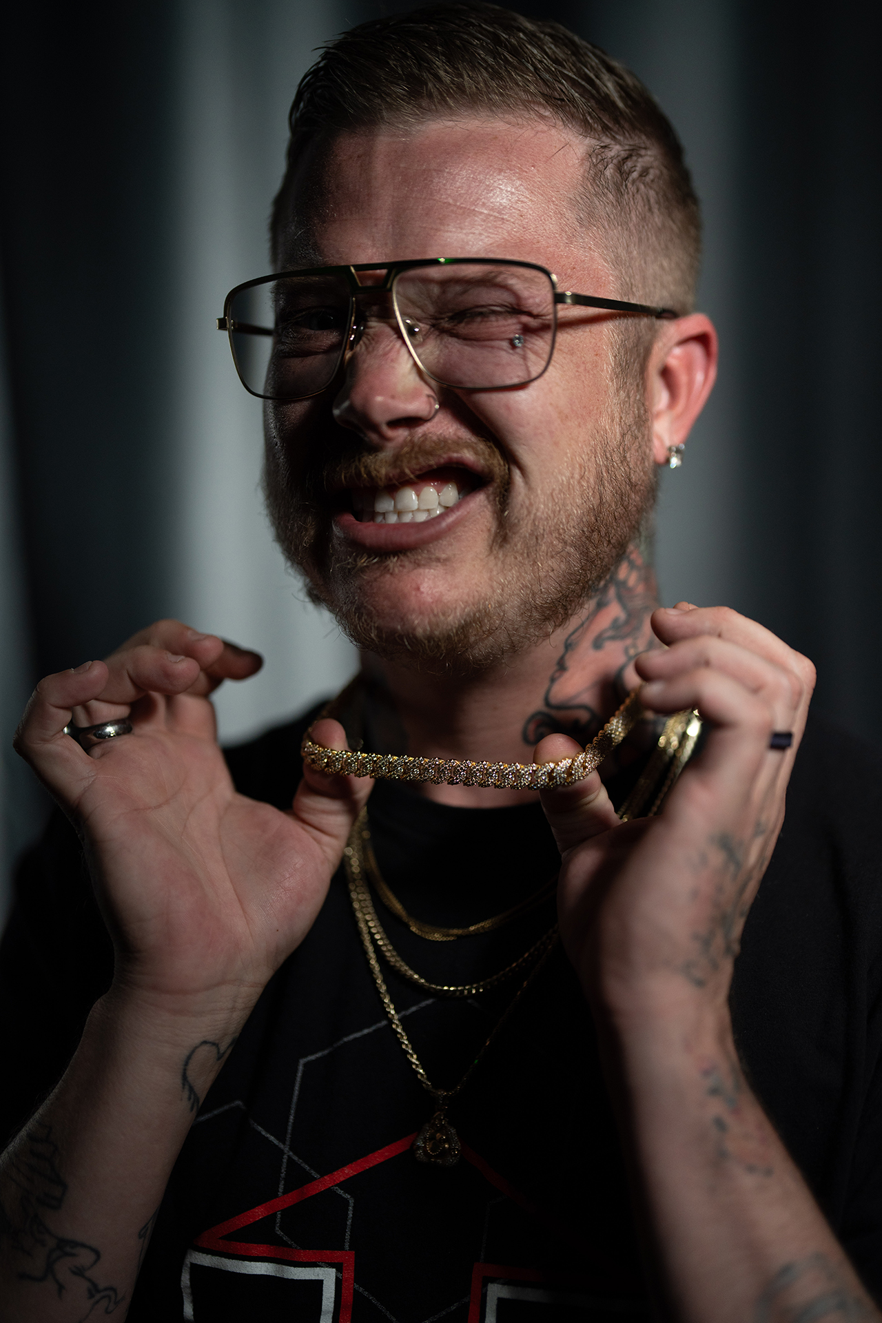Portrait of a smiling tattoo artist wearing glasses and layered chain necklaces