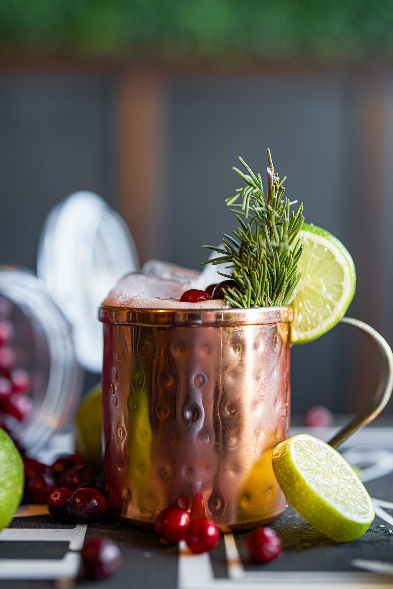 Yule Mule cocktail in a copper mug garnished with rosemary, lime, and cranberries, at Pretty Neat Bar